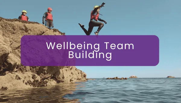 A person joyfully jumping into the water from a rock with onlookers, under the text 'Wellbeing Team Building'
