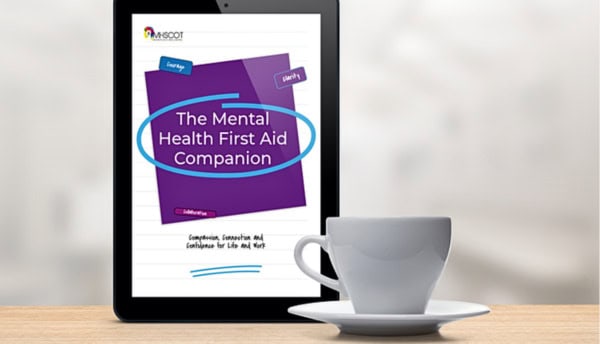 Cover of The Mental Health First Aid Companion guide on a tablet screen with a coffee cup.
